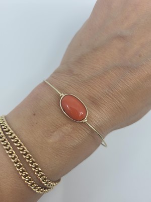Lot 59 - A CORAL SET BANGLE, the bezel set cabochon...